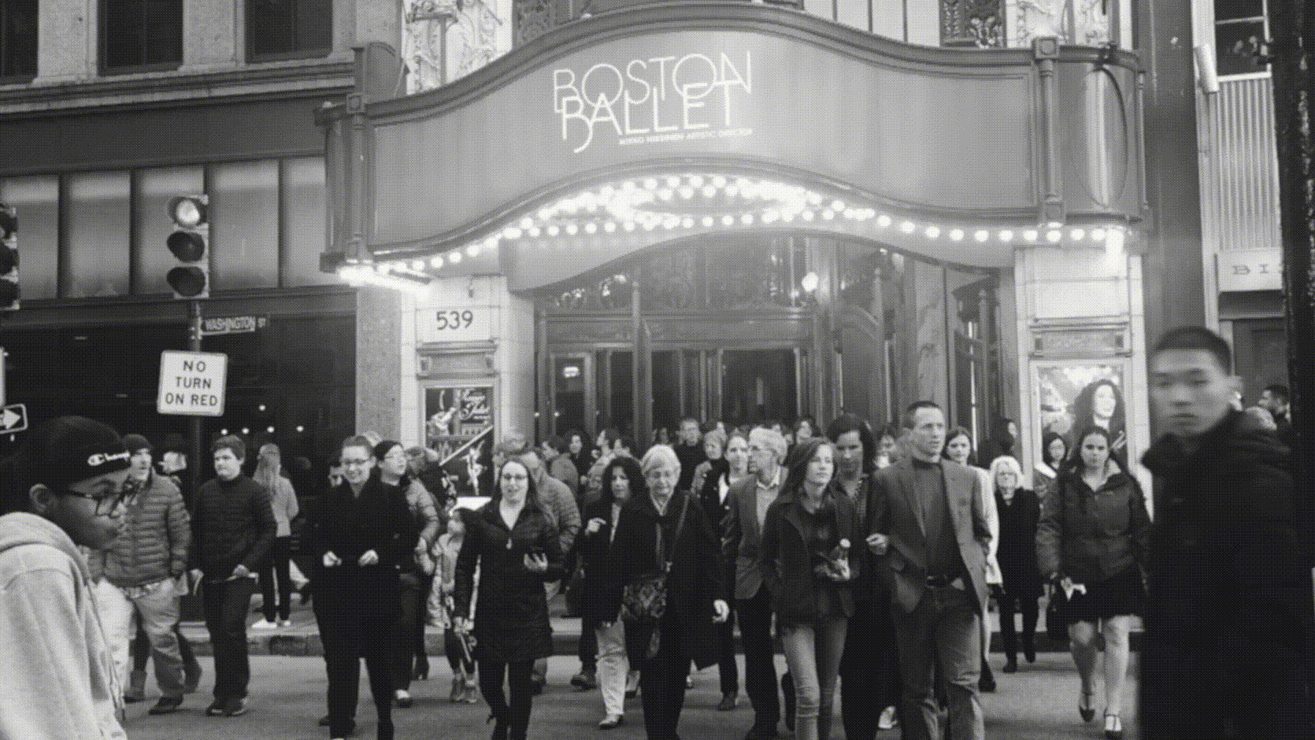 This moving gif is in black and white and shows a crowd of people pouring out of the front doors of Paramount Theater after the end of a show.