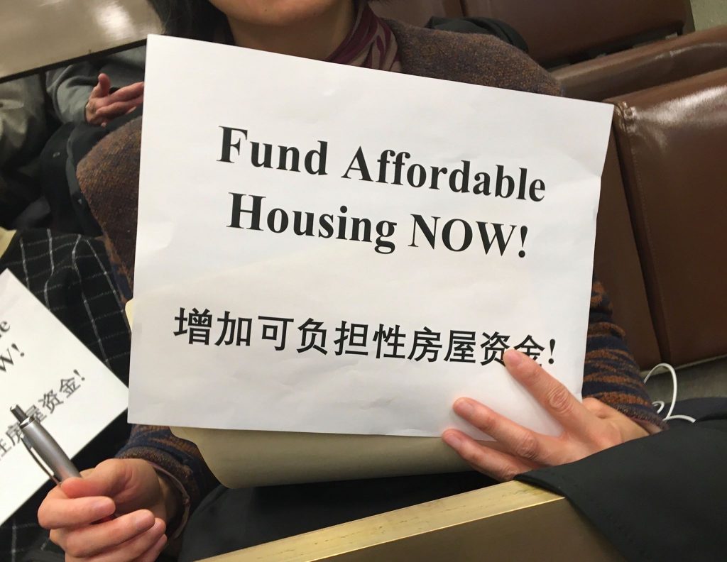 Silent protestors in the crowd held signs that said "Fund Affordable Housing NOW!" Photo by Joseph Handel.