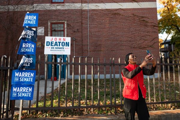 Nov. 5, 2024 — Reneé, a volunteer poll worker, takes a video of herself in front of the polling place, encouraging her freinds, family, and social media followers to get out to the polls and votes. She has been working on election day for 7 years, the past 4 years in Massachusetts. Photo by Faith Nguyen.