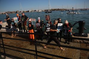 Activists from a coalition of climate organizations, including Extinction Rebellion Boston and Mothers Out Front, stand in rising harbor water as the King Tide flushes through the concrete wall at Long Wharf on Saturday, Oct. 19, 2024.